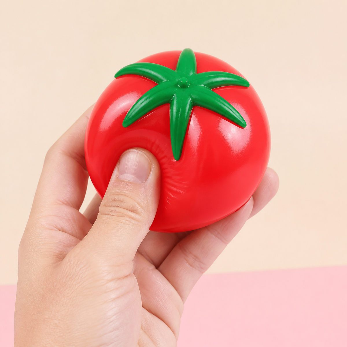 Hand gently squeezing the Tomato Splat Squeeze Toy